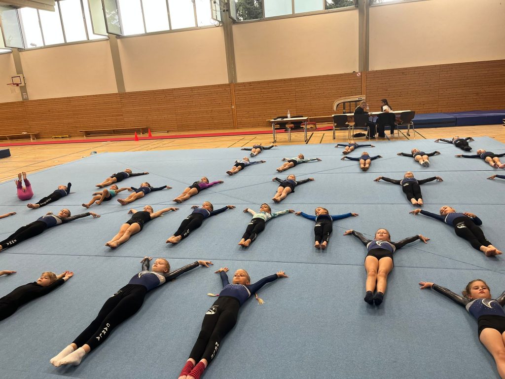 Viele Turnerinnen liegen auf der Bodenfläche und absolvieren ihr Aufwärm-Programm.