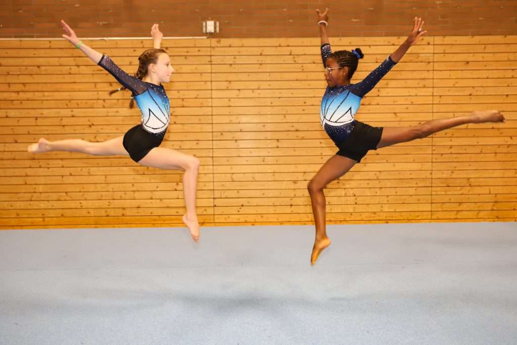 Bild von der Seite. Zwei Turnerinnen springen aufeinander zu.