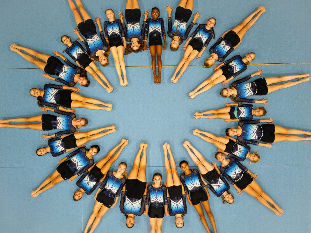 Gruppenbild von oben. Ca. 30 Turnerinnen liegen im Kreis auf der blauen Bodenfläche.