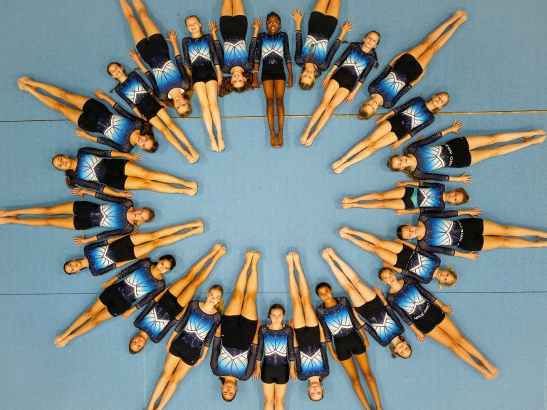 Gruppenbild von oben. Ca. 30 Turnerinnen liegen im Kreis auf der blauen Bodenfläche.
