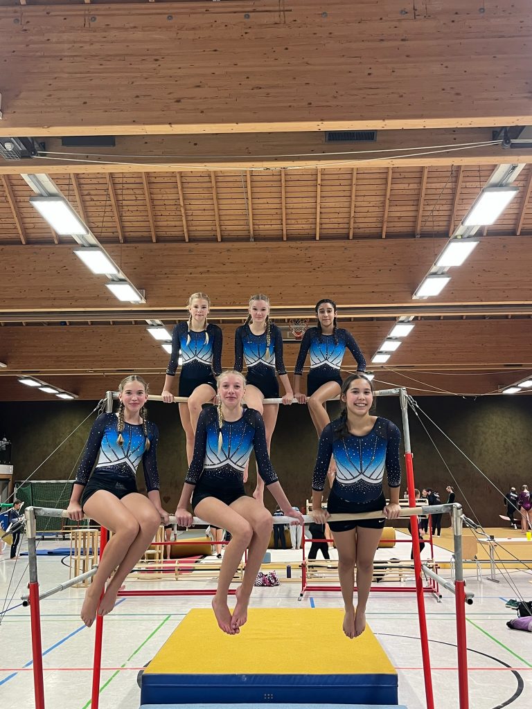 Sechs Turnerinnen sitzen nebeneinander auf den beiden Holmen des Stufenbarrens.