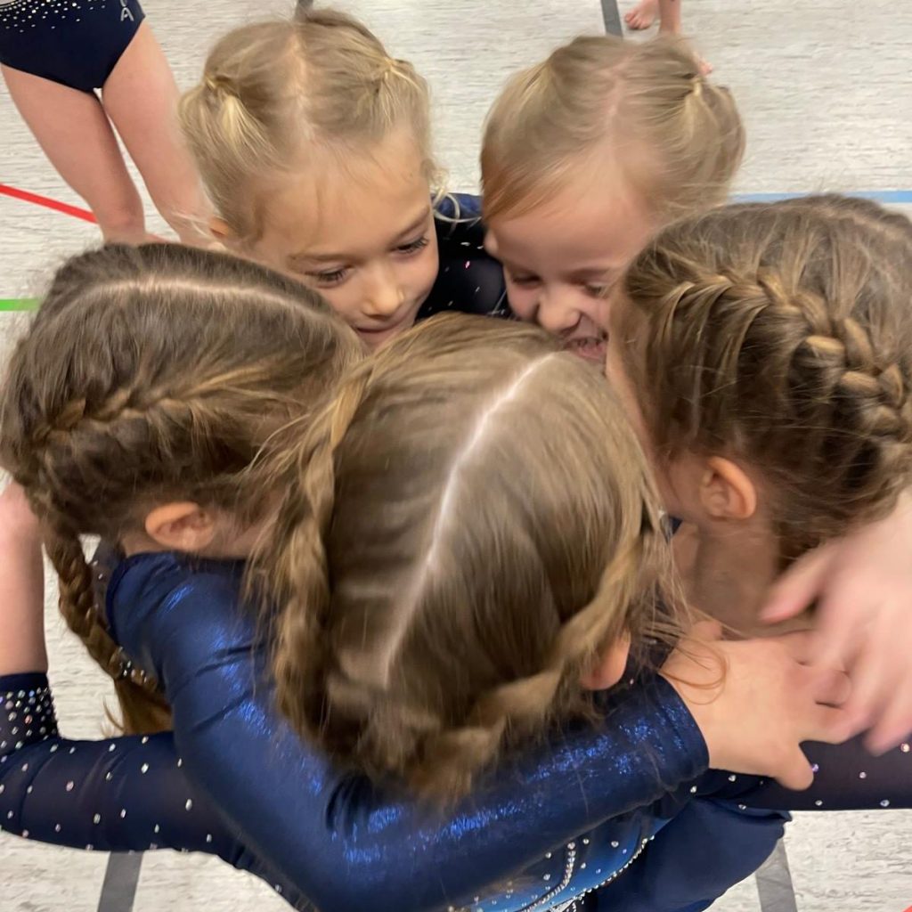 5 Turnerinnen stehen dicht gedrängt zusammen und umarmen sich gegenseitig. Blick von schräg oben auf ihre Köpfe.