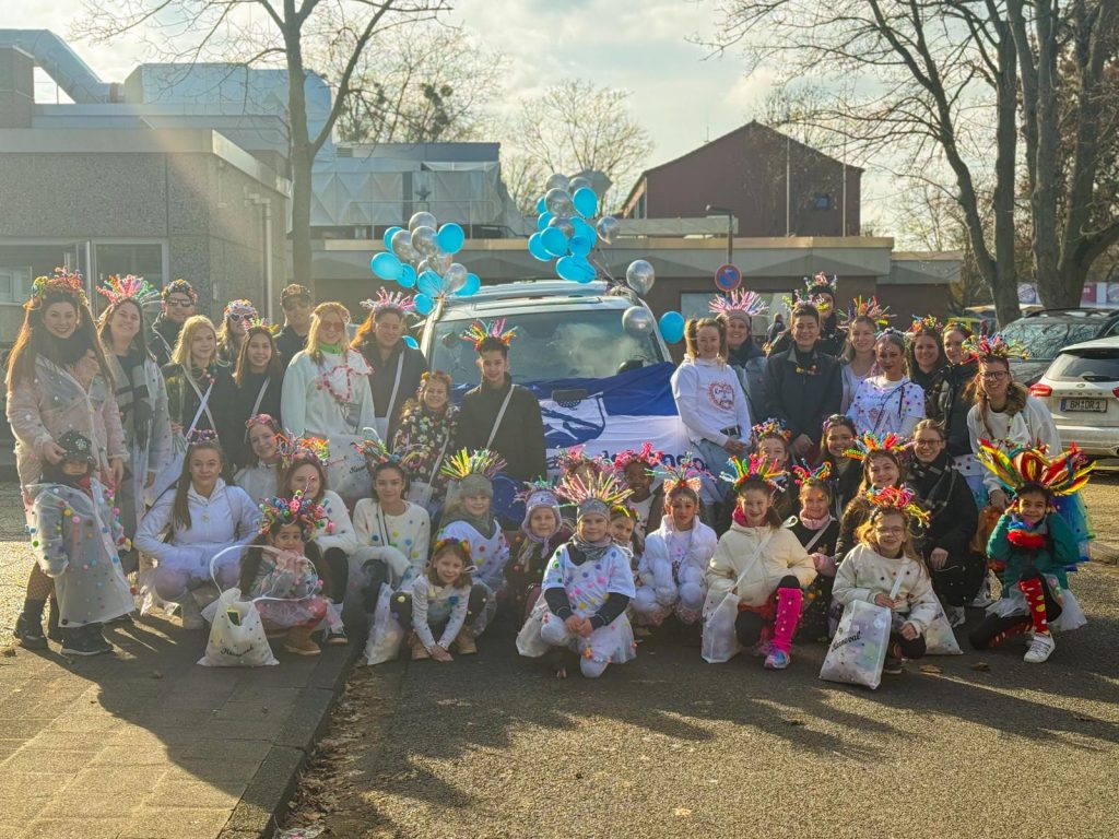 Gruppenfoto: Alle Teilnehmenden in bunten Konfetti-Kostümen vor einem mit Vereinsfahne und blauen und silbernen Luftballons geschmückten Auto.