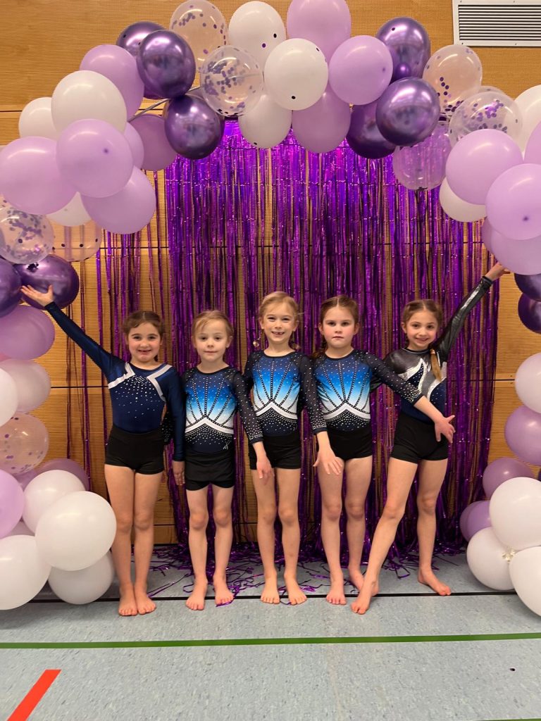 5 Turnerinnen stehen unter einem Luftballonbogen und lächeln in die Kamera.