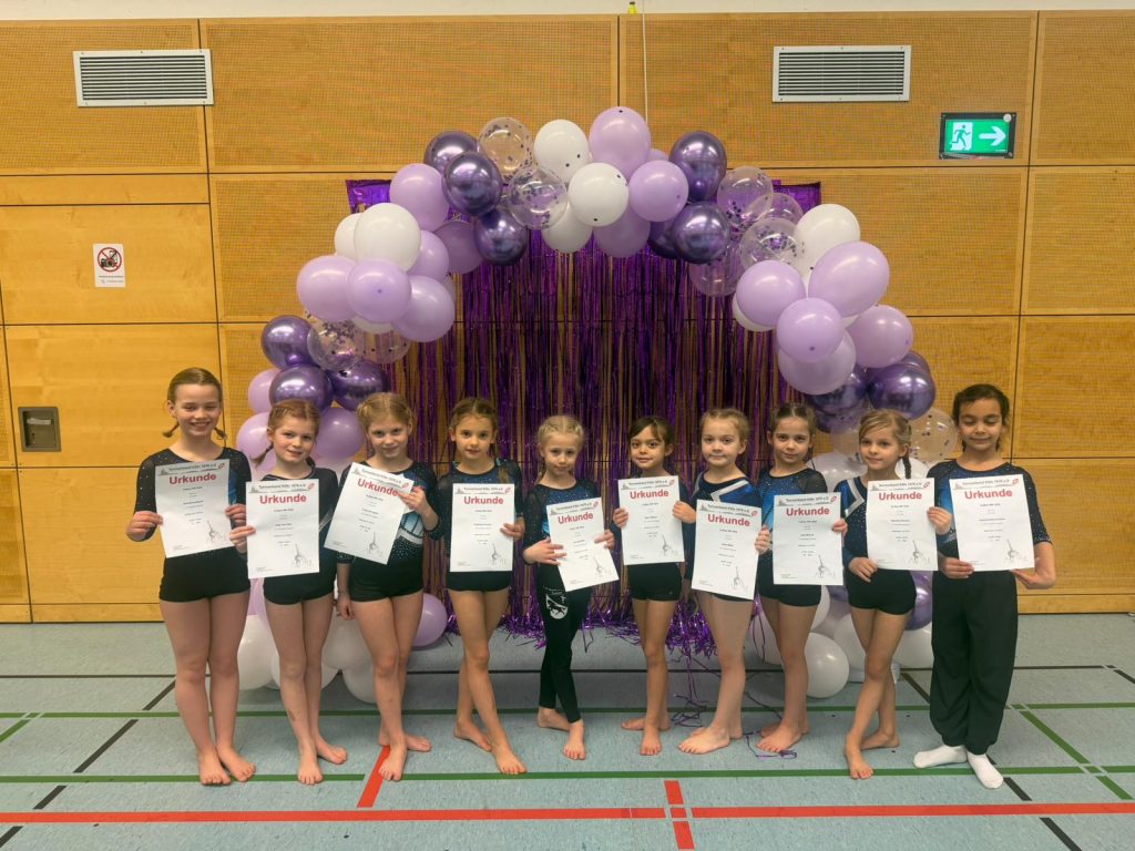 10 Turnerinnen stehen mit ihren Urkunden vor einem Luftballonbogen und lächeln in die Kamera.