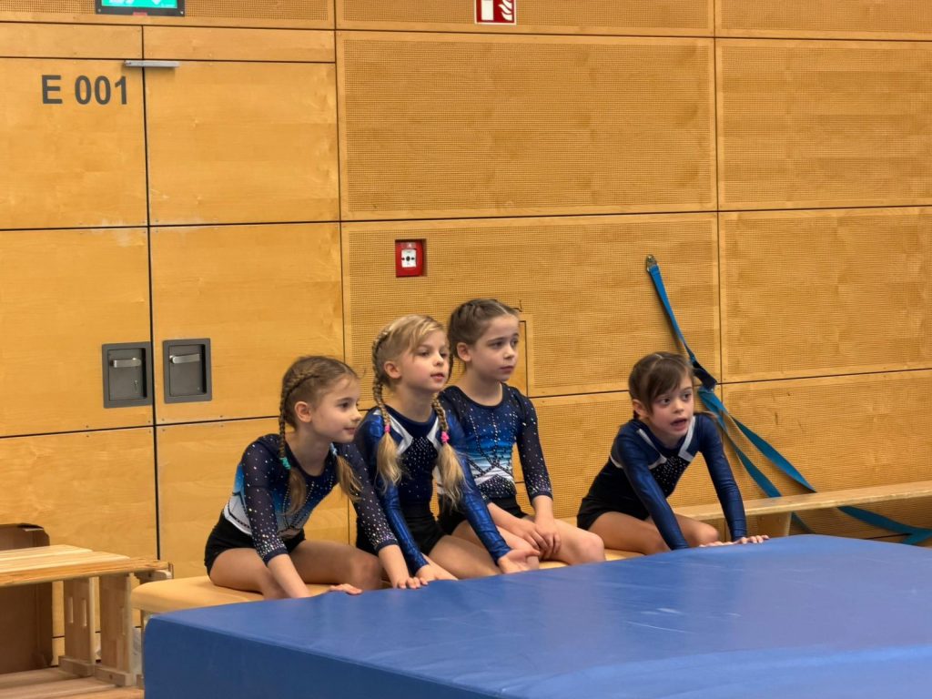 4 Turnerinnen sitzen auf einem Kasten und beobachten etwas.