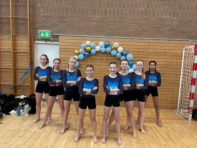 8 Turnerinnen stehen vor einem Luftballonbogen und lächeln in die Kamera.