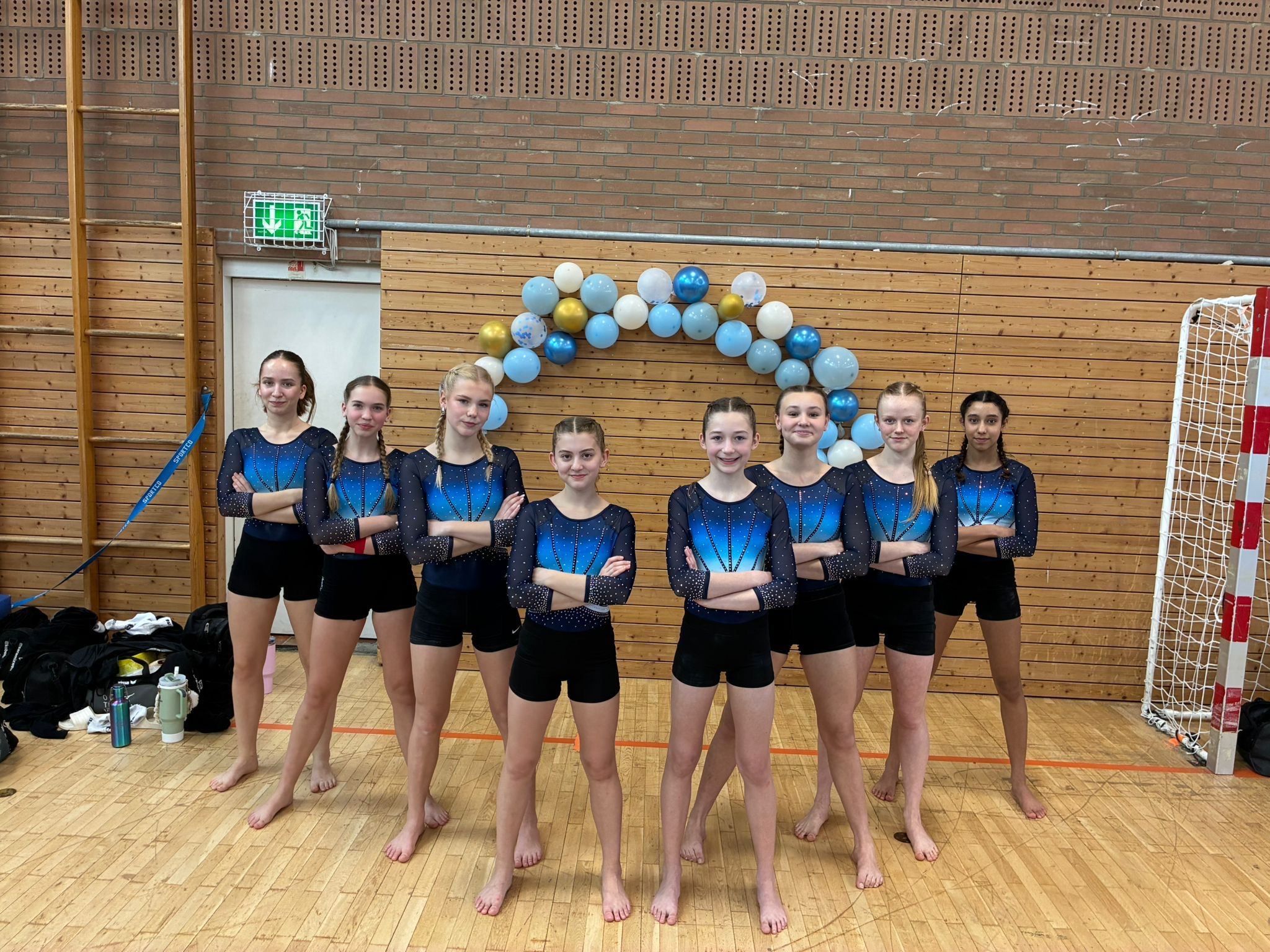 8 Turnerinnen stehen vor einem Luftballonbogen und lächeln in die Kamera.