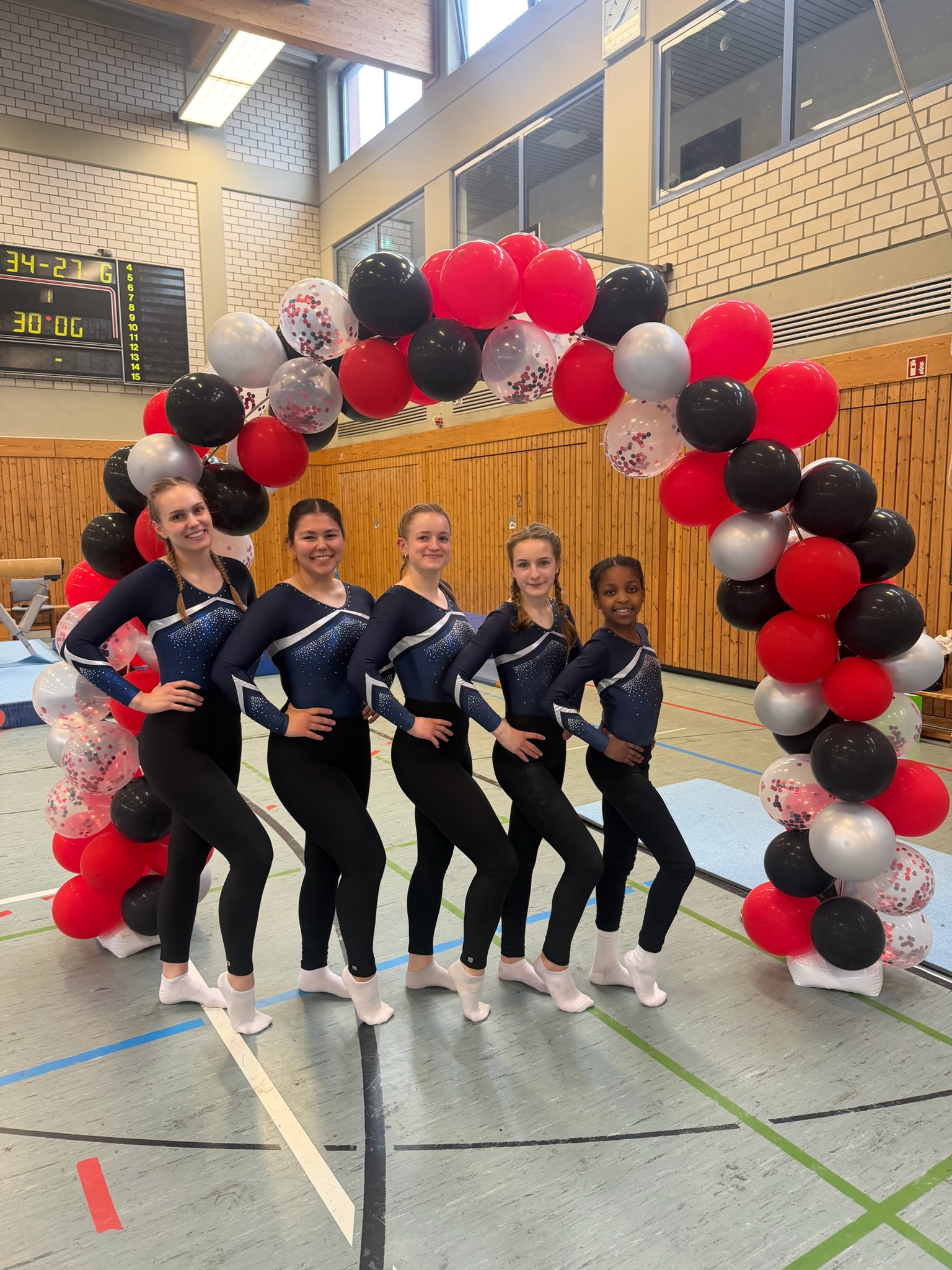 5 Turnerinnen stehen vor einem Luftballonbogen und lächeln in die Kamera.